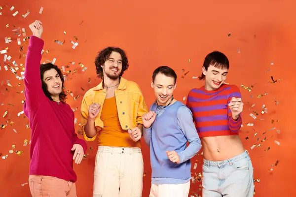 Чотири молоді веселі геї в яскравому одязі позують разом під дощем конфетті, місяць гордості — стокове фото
