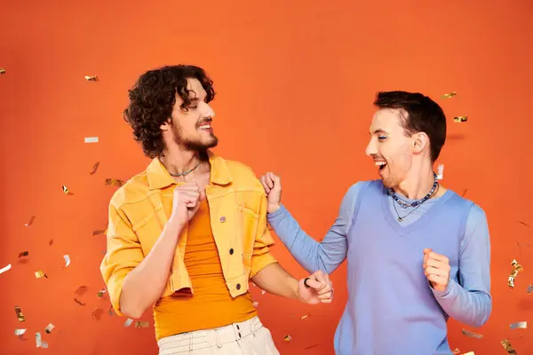 Positive good looking gay friends in stylish clothes with makeup posing under confetti rain, pride — Stock Photo