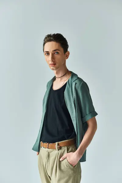 Ein junger Mann posiert stolz in grünem Hemd und brauner Hose und präsentiert seine lebendige queere Mode in einem Studio-Setting. — Stockfoto