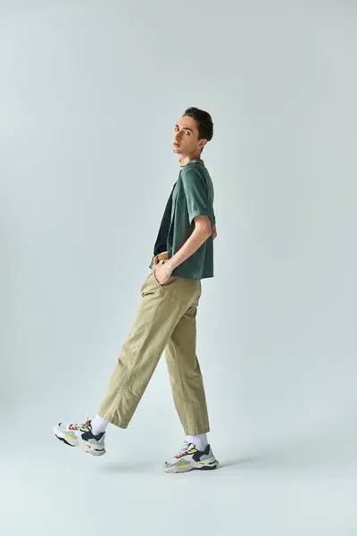 Una joven queer posa con confianza en un estudio, con una elegante camiseta y pantalones caqui sobre un fondo gris. — Stock Photo