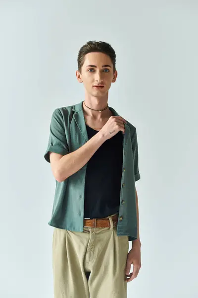 Une jeune queer posant en toute confiance dans un studio, portant une chemise verte élégante et un pantalon bronzé sur un fond gris. — Photo de stock