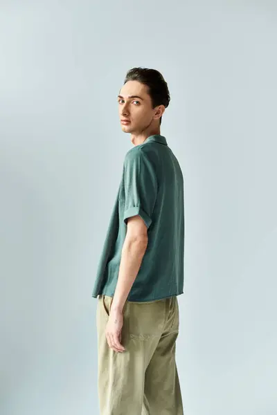Jeune queer pose fièrement dans un polo vert et un pantalon kaki sur fond de studio gris. — Photo de stock