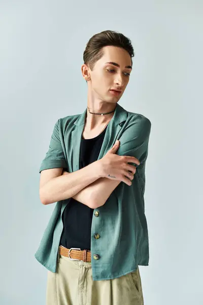 Una joven queer posa confiadamente en un estudio con una camisa verde y pantalones bronceados, expresando orgullo LGBT sobre un fondo gris. — Stock Photo