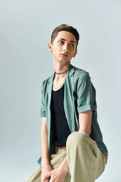 Молода квір-людина впевнено позує в яскраво-зеленій сорочці і засмагає штани на сірому студійному фоні. — стокове фото