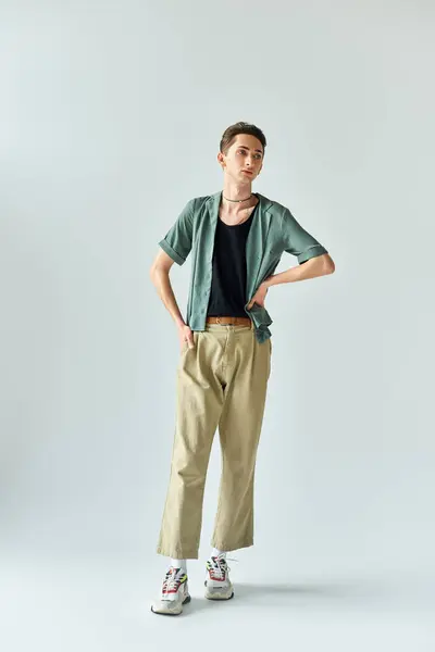 Junge queere Person posiert selbstbewusst im Studio mit braunem Hemd und khakifarbener Hose vor grauem Hintergrund. — Stockfoto