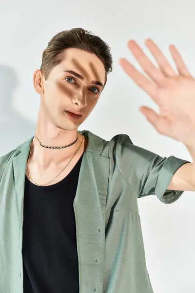A young queer man in a green shirt strikes a hand gesture, showcasing pride and individuality in a studio setting on a grey background. — Stock Photo