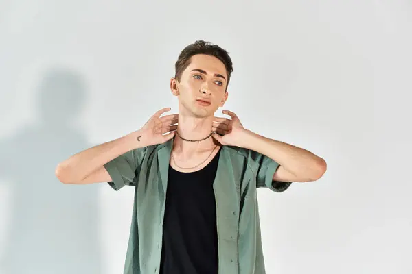 A young queer person confidently poses in a studio wearing a green shirt against a grey background. — Stock Photo