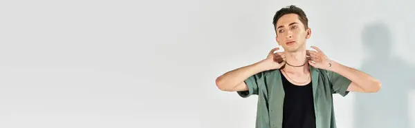 Una joven queer posa confiadamente con las manos en la cabeza en un estudio sobre un fondo gris. — Stock Photo