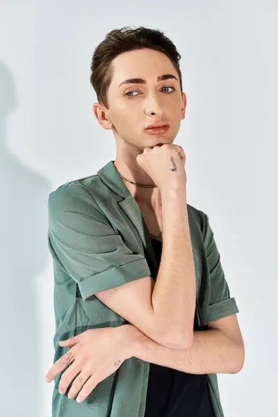 A young man in a green shirt strikes a pensive pose, hand resting on chin, exuding style and confidence in a studio setting. — Stock Photo