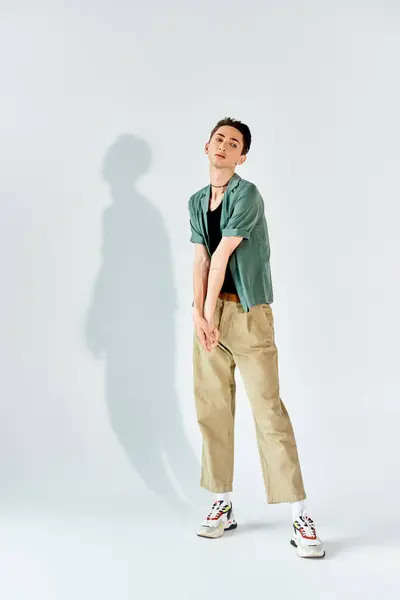 A young queer person strikes a stylish pose in a tan shirt and khaki pants, exuding confidence in front of a white background. — Stock Photo