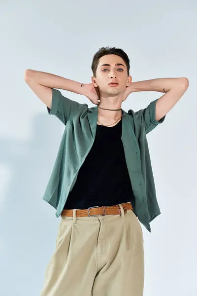 Eine junge queere Person posiert selbstbewusst in einem Studio-Setting, trägt ein stylisches grünes Hemd und eine khakifarbene Hose vor grauem Hintergrund. — Stockfoto