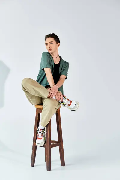 Un jeune queer assis élégamment sur un tabouret dans un studio, montrant confiance et fierté. — Photo de stock