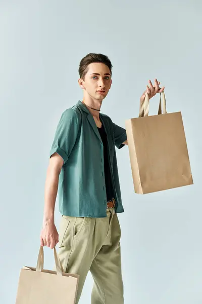 A young queer person joyfully holds shopping bags against a vibrant blue background. — Stock Photo