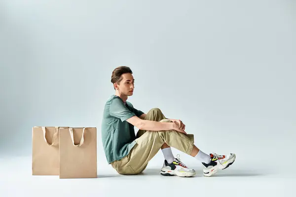 Un hombre, abrazando la terapia comercial, se sienta en el suelo rodeado de bolsas de compras. — Stock Photo