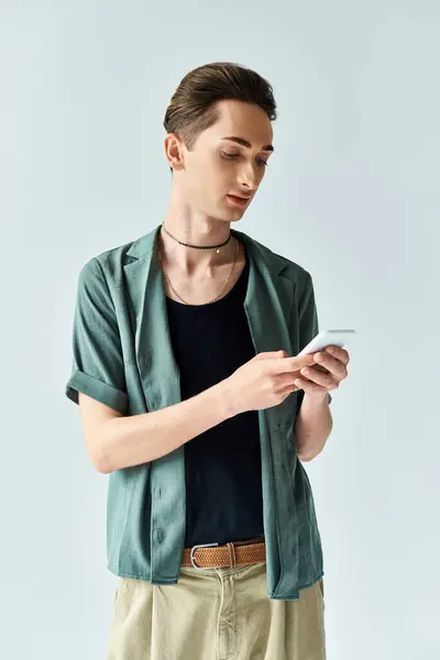 Ein stilvoller junger queerer Mann in grünem Hemd und brauner Hose checkt vor grauer Studiokulisse sein Handy. — Stockfoto