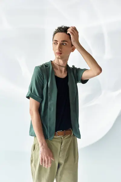 Un giovane omosessuale con orgoglio indossa una camicia verde e pantaloni kaki, posando con fiducia in uno studio ambientato su uno sfondo grigio. — Foto stock