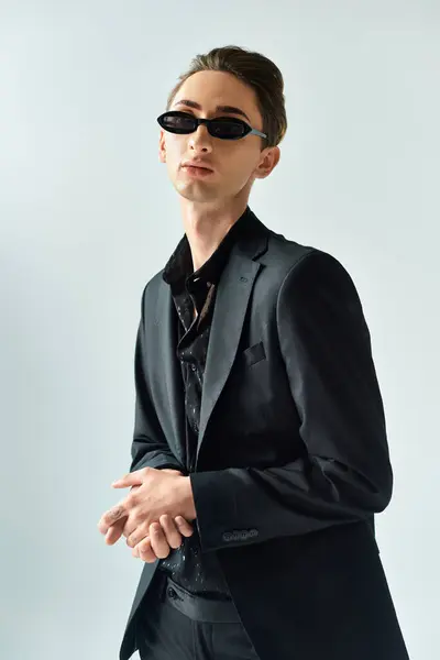 A stylish queer person in a suit and sunglasses strikes a pose in a studio against a grey background, embodying LGBT pride. — Stock Photo