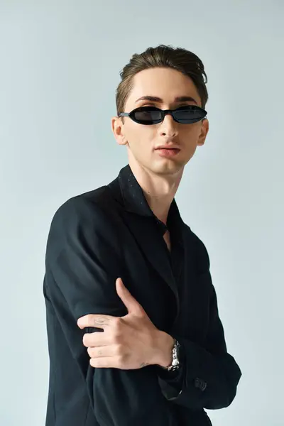 Ein junger, queerer Mensch in schickem Anzug und Sonnenbrille posiert selbstbewusst vor grauem Hintergrund. — Stockfoto