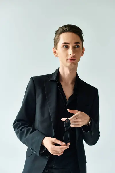 A young queer person in a stylish black suit strikes a confident pose against a grey studio backdrop. — Stock Photo