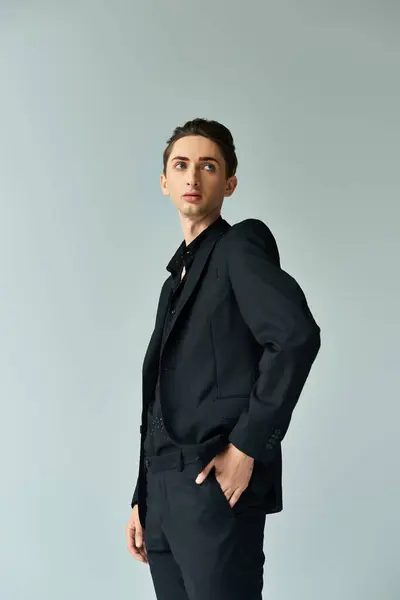 A young queer person strikes a confident pose in a sleek black suit against a grey backdrop, exuding pride and style. — Stock Photo