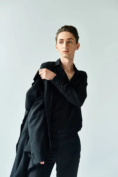 Um jovem gay posa confiantemente em um elegante terno preto em um estúdio contra um fundo cinza. — Fotografia de Stock