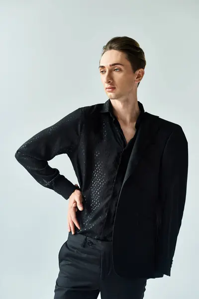 A young queer person strikes a pose in a stylish black suit against a grey studio backdrop, exuding confidence and pride. — Stock Photo