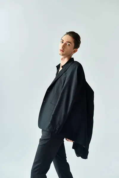 A young queer person exudes confidence in a black blazer and pants, posing elegantly on a grey studio background. — Stock Photo