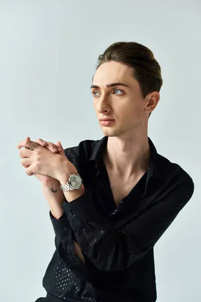 Un joven con una camisa negra muestra con confianza su orgullo queer mientras posa en un estudio sobre un fondo gris. — Stock Photo