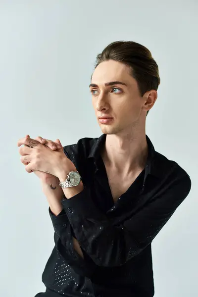 A young man in a black shirt confidently displays his queer pride as he strikes a pose in a studio against a grey background. — Stock Photo