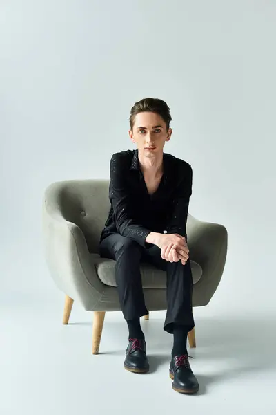 A young queer person confidently sits on a gray chair in a studio setting, exuding pride and self-assurance. — Stock Photo