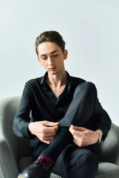 Un giovane seduto su una sedia che si lega le scarpe, con un focus sull'orgoglio e l'espressione di sé. Studio girato su sfondo grigio. — Foto stock