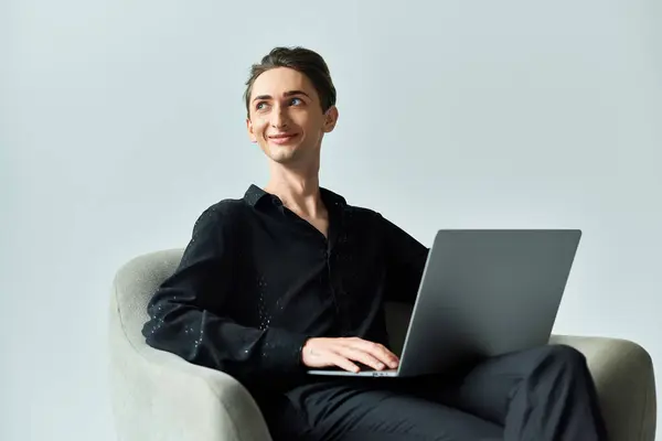 Una joven queer sobre un fondo gris se sienta en una silla con un portátil, exudando confianza y orgullo por su presencia digital. — Stock Photo