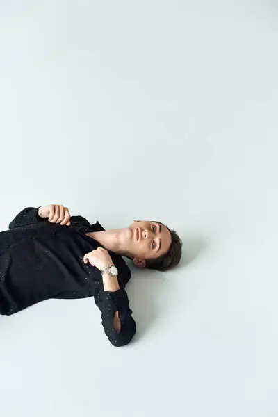 Un giovane omosessuale giace sul suo stomaco, trasudando tranquillità e introspezione, su uno sfondo bianco duro. — Foto stock