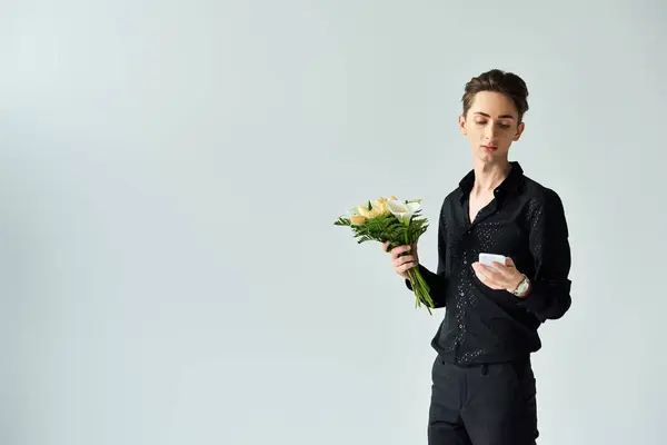 A young queer person holding a bouquet of flowers in a studio setting on a grey background. — Stock Photo