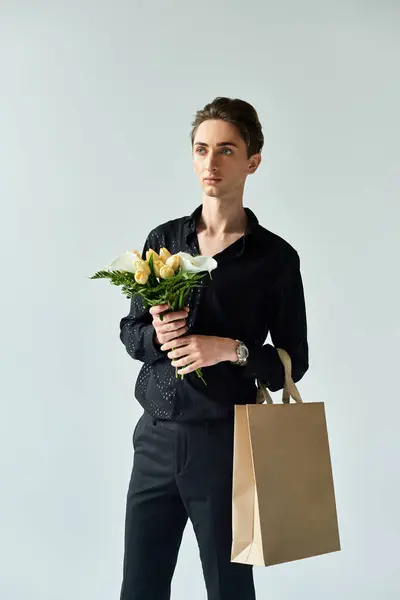 A young queer man elegantly holds a paper bag filled with vibrant flowers, radiating pride in a studio setting. — Stock Photo