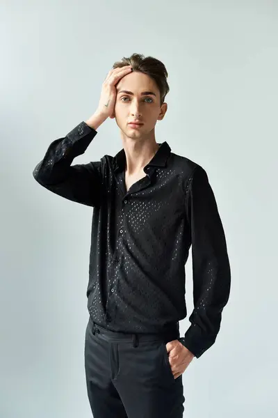 A young queer person in a black shirt and pants strikes a pose against a grey backdrop in a studio setting. — Stock Photo