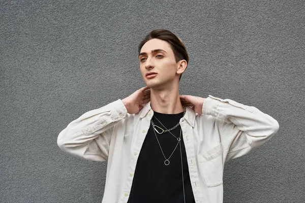 Un joven queer posa confiadamente contra una pared gris, mostrando su elegante atuendo con orgullo y confianza. — Stock Photo