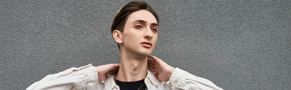 Un joven queer toma una postura orgullosa frente a una pared gris, mostrando su elegante atuendo y celebrando el orgullo LGBT. — Stock Photo