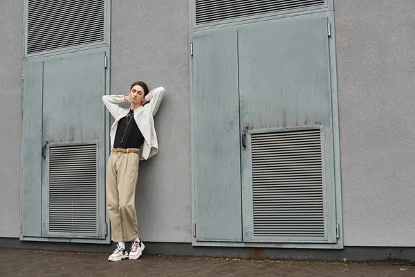 A stylish young queer person leans confidently against a wall, exuding pride and individuality. — Stock Photo