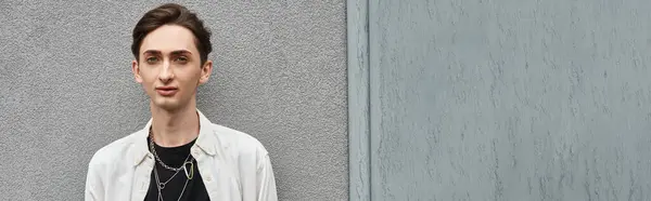 Ein junger queerer Mensch in schicker Kleidung steht mutig vor einer grauen Wand und strahlt Stolz und Trotz aus.. — Stockfoto