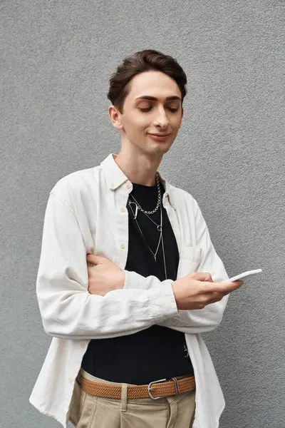 Un joven con un atuendo elegante, que representa el orgullo LGBT, sostiene un teléfono celular. - foto de stock