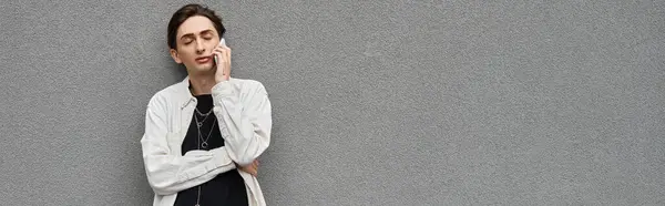 Une jeune queer en tenue élégante se penche nonchalamment contre un mur gris, respirant confiance et fierté. — Photo de stock