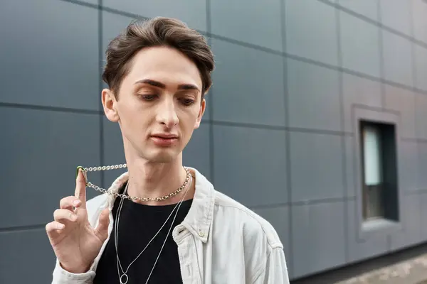 Um jovem elegante segura um colar na frente de um edifício majestoso, mostrando seu senso único de moda e orgulho. — Fotografia de Stock