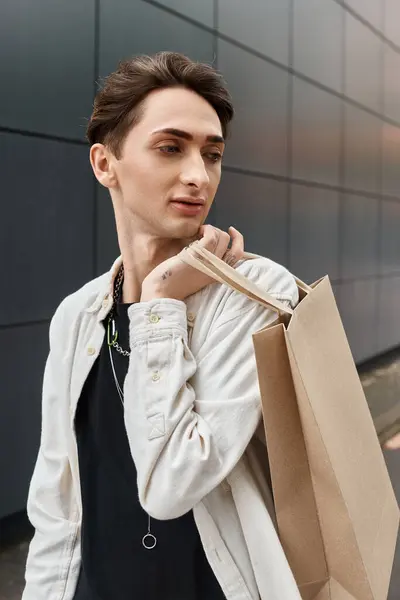 A stylish young individual with a shopping bag stands in front of a modern building. — Stock Photo