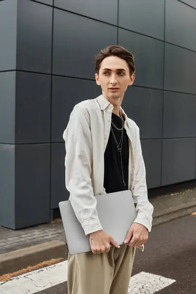 Um jovem queer elegante indivíduo orgulhosamente detém um laptop fora de um edifício moderno em um ambiente urbano. — Fotografia de Stock