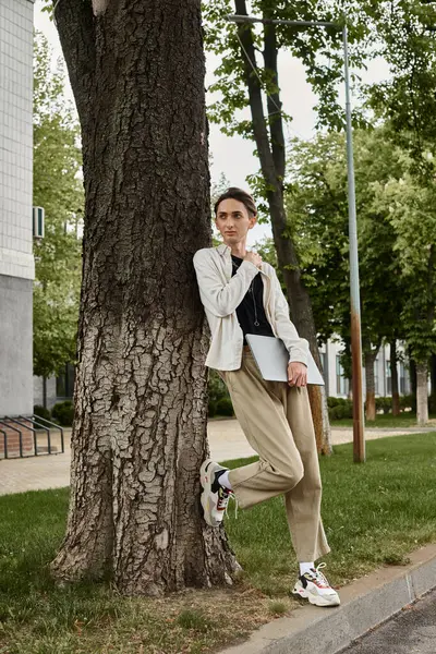 Um jovem queer individual em trajes elegantes se inclina pensativamente contra uma árvore, incorporando orgulho e contemplação. — Fotografia de Stock