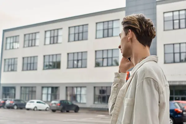 A young queer individual in fashionable attire talking on his cell phone in front of an urban building, showcasing LGBTQ pride. — Stock Photo