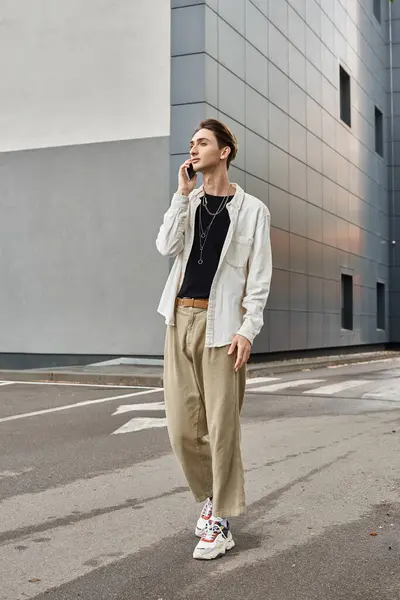 A stylish young queer individual in vibrant attire stands in front of a building, talking on his cell phone. - foto de stock