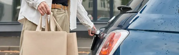 Um jovem gay em trajes elegantes segurando sacos de compras ao lado de um carro azul — Fotografia de Stock