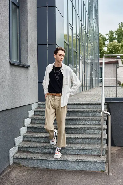 Молода квір-людина, вкладена в стильний одяг, вдаряє впевнену позу на сходах будівлі. — стокове фото